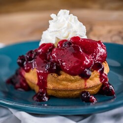 A Belgian waffle topped with whipped cream and a berry compote