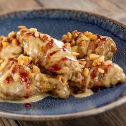 A plate of chicken wings topped with a peanut sauce