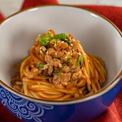 A bowl of dandan noodles topped with spicy pork, sesame seeds and sliced green onions