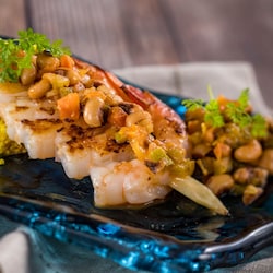 A skewer of grilled shrimp topped with beans, served over a bed of couscous