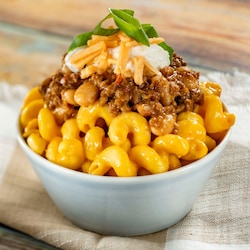 A small bowl of macaroni and cheese topped with chili, sour cream and cheddar cheese