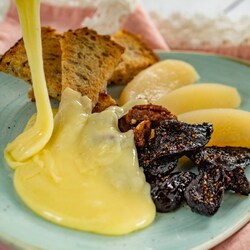 A plate featuring melted Swiss cheese served with 3 slices of pear, braised figs and wedges of toast