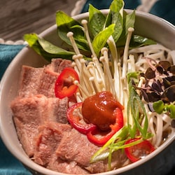 A bowl of traditional spicy Vietnamese pho, featuring shaved beef, mushrooms, peppers and thai basil