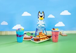 An assortment of food and beverages is displayed, featuring frozen drinks, pastries with dipping sauces, a decorated dessert and a Bluey souvenir cup