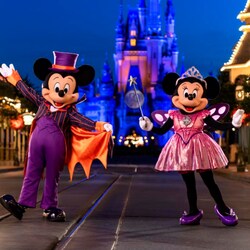 Mickey Mouse vestido como un vampiro y Minnie Mouse vestida como una princesa de hadas, parados cerca de Cinderella Castle en la noche