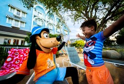 A child smiling in excitement as they greet Goofy while sitting near the pool at Disney’s Beach Club Resort