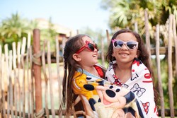 2 girls wrapped in beach towels wearing sunglasses while hugging each other