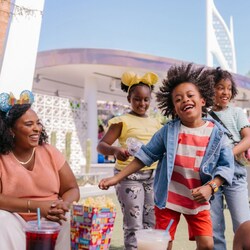 Three children dance and play as 2 adult family members look on, next to the Downtown Disney Live Stage