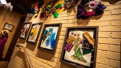 A hallway with framed clothing designs and Mardi Gras masks hung on the wall.