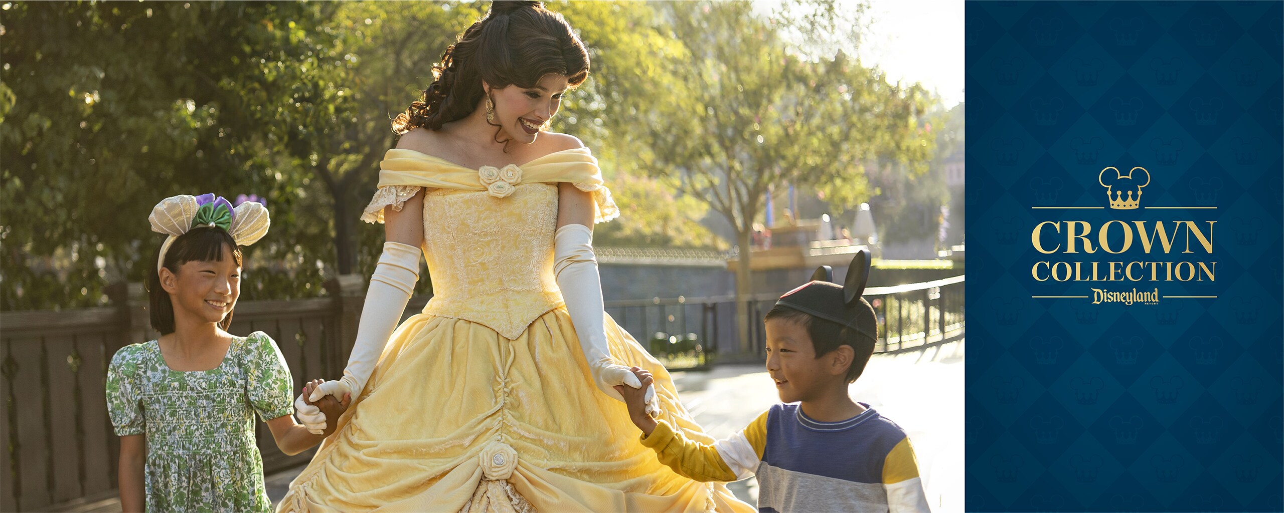 Two smiling children wearing Ear Headbands and holding hands with Belle, with text that says, ‘Crown Collection Disneyland Resort’