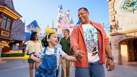 A young girl wearing a Minnie Mouse headband walking with her dad through Disneyland Park with Sleeping Beauty Castle in the background