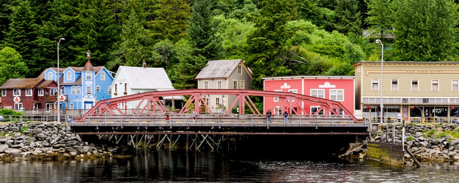 A bridge extends over a small inlet with buildings and woods in the background