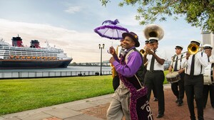A man in cheery attire with a fluffy parasol leads a small band of musicians past a Disney cruise ship