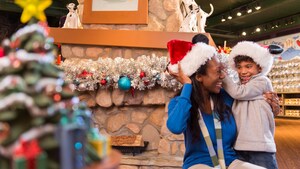 A mother and son wearing Santa hats in a store decorated with a holiday wreath and a Christmas tree 