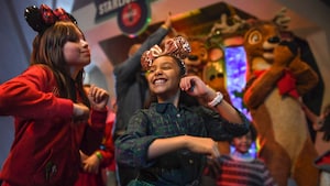 Two girls wearing Mickey ears dance while reindeer stand in the background