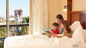 A woman reads to 2 children in a bed near a window with a view of Guardians of the Galaxy Mission  BREAKOUT