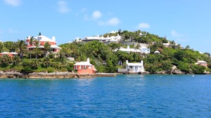 A shoreline pressed up against a grassy hill with buildings and trees