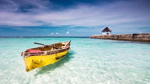 An old rowboat floats in clear waters next to a breaker with a small gazebo structure