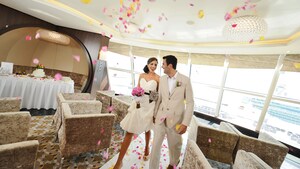 A bridesmaid holding a bouquet walks down a wedding aisle on a ship deck with a groomsman