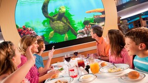 A father and son dine under an animation screen depicting a sea turtle