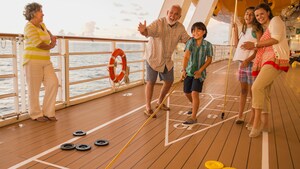 A grandfather and grandmother playing shuffle board with their 3 grandchildren on board the deck of a cruise ship