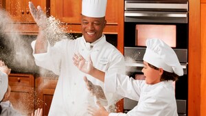 A man and a child in chef attire throw flour in the air