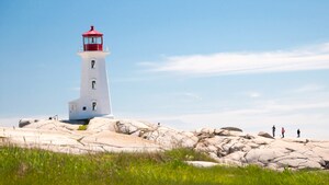 A lighthouse on a craggy rock cliff with a few people nearby