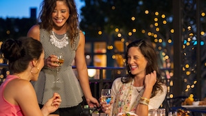 3 women laugh as they drink at a table