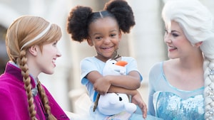Una Visitante sonríe mientras abraza un peluche de Olaf en un encuentro con Personajes, con Anna y Elsa