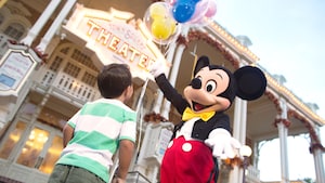 Mickey Mouse ofreciendo un manojo de globos a un joven Visitante en el Parque Temático Magic Kingdom