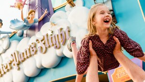 A young female Guest laughs while being held up in the air by her dad outside of Peter Pan’s Flight