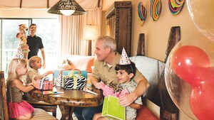 With children and parents looking on, a little boy unwraps birthday gifts at a party