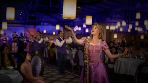 Rapunzel and Cast Members walk down an aisle displaying glowing lanterns as Guests watch