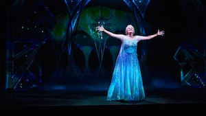 On stage, a live performance of a play inspired by Disney's 'Frozen,' with Elsa singing in a forest