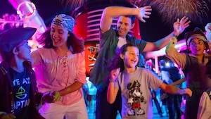 A family dancing on the deck of a cruise ship as fireworks explode overhead