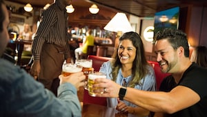 Three Guests clinking glasses of beer together while sitting at a table in a bar