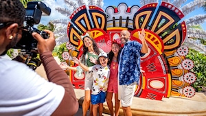 Una familia de cuatro personas posa para una foto frente a un telón de fondo llamativo inspirado en un festival durante una aventura tropical de Disney Cruise Line.