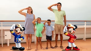 Una familia joven de cuatro personas saltando en la cubierta de un barco de Disney junto a figuras ilustradas de los capitanes Mickey Mouse y Minnie Mouse