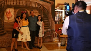 Un fotógrafo tomando una foto de una familia joven de cuatro personas frente a un telón de fondo con un estilo de un barco de madera antiguo
