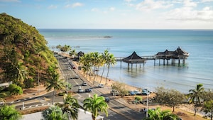 Un entorno tropical con un camino costero, un muelle y cabañas sobre el agua