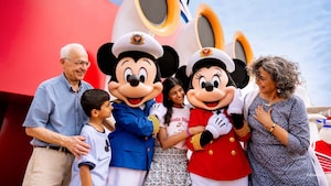 Cuatro Huéspedes posan con los Capitanes Mickey y Minnie frente a las sirenas de niebla en un barco de Disney Cruise Line