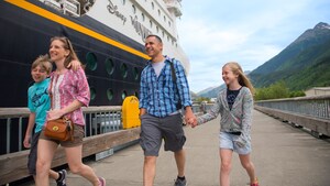 A family of 4 walk on a platform alongside a Disney Cruise Line ship
