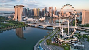 An aerial view of Singapore at sunset, featuring the Singapore Flyer Ferris wheel, Marina Bay Sands and reflections in the calm bay water
