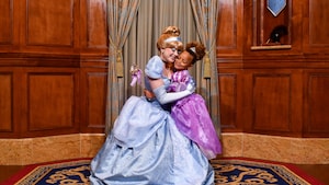 A young girl dressed like a princess hugs Cinderella