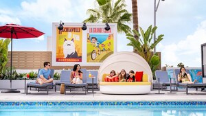 At the rooftop Pixel Pool area at Pixar Place Hotel, adults sitting in lounge chairs and 3 kids relaxing on a day bed, surrounded by vibrant artwork depicting Pixar stories