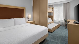 A hotel resort suite bedroom with a bed, dresser, desk, TV and a bunk bed with 3 mattresses