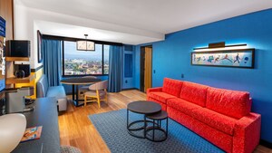 A hotel suite living area with a couch, dining table, window and Pixar themed artwork