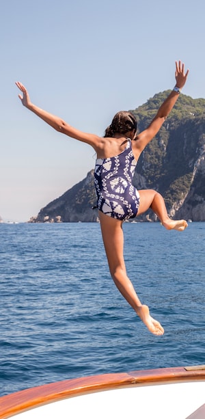 A young girl jumping off the edge of a sail boat into the ocean