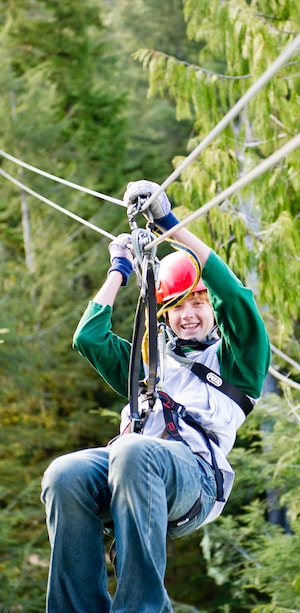 A teenage boy smiles while gliding through a forest on a zip line