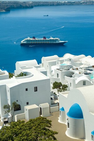 A Disney cruise ship sailing next to a Greek coastal town 